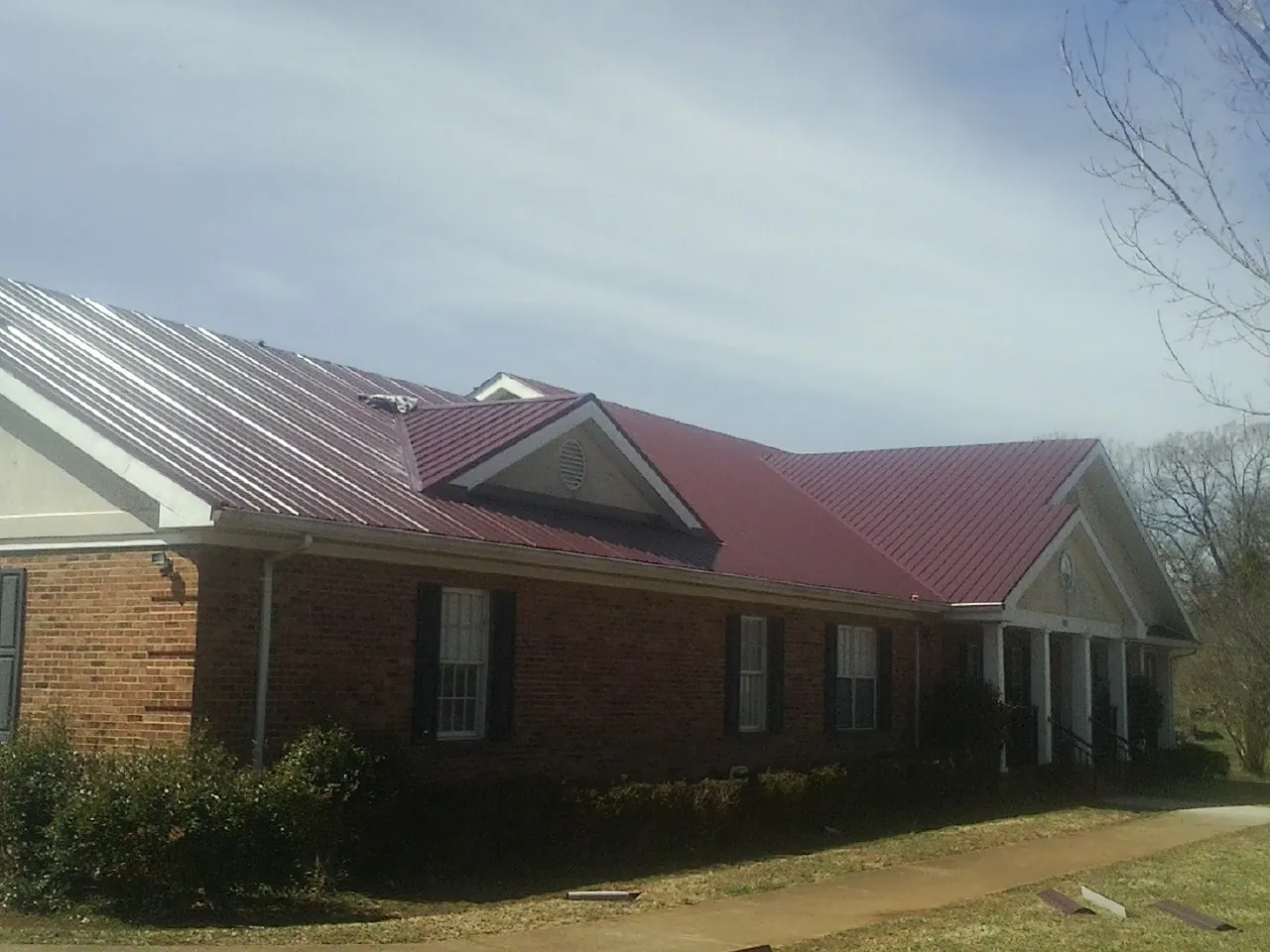 Red metal roof with gabled entries on a long brick building, from a Hail Damage Roof Repair job in Andersonville