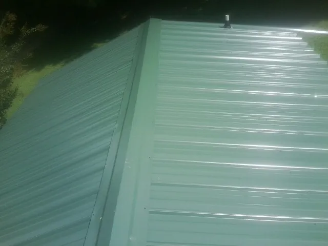 New green metal panels meeting at the ridge of a roof — Flat Roof Repair work by our crew in Andersonville